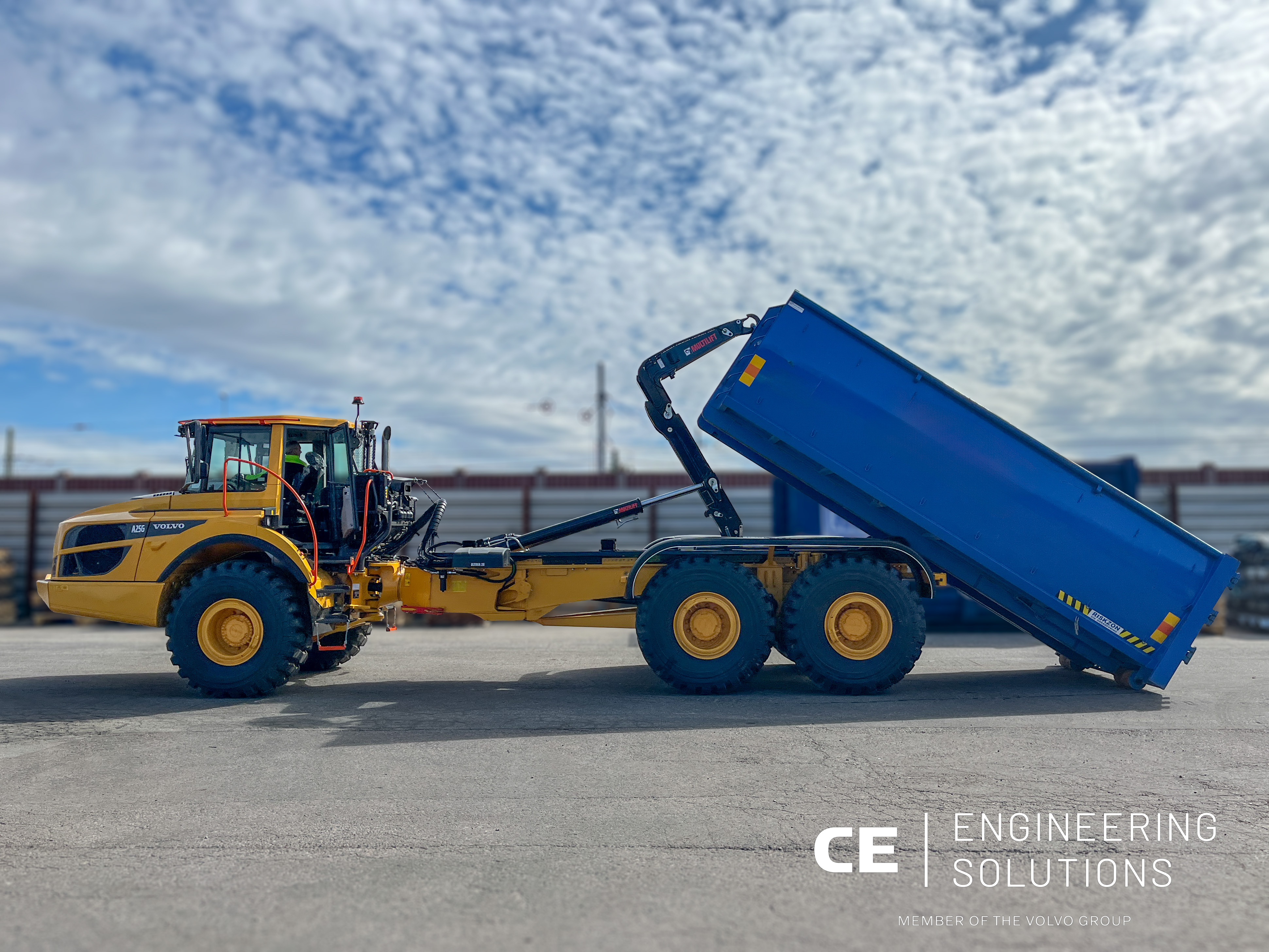 A yellow dump truck with a raised blue bed at a construction site